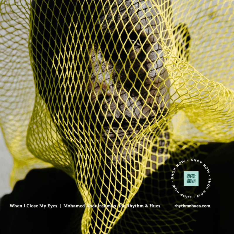 Man poses in sunlight presenting shadows as they poke through the mesh holes of yellow artistic facial covering